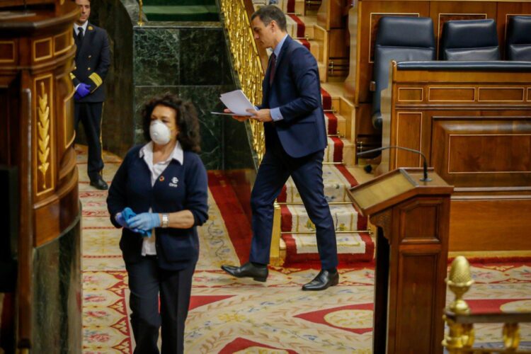 Mujer con mascarilla y guantes limpia la sala del Congreso mientras un hombre se dirige a la tribuna de oradores