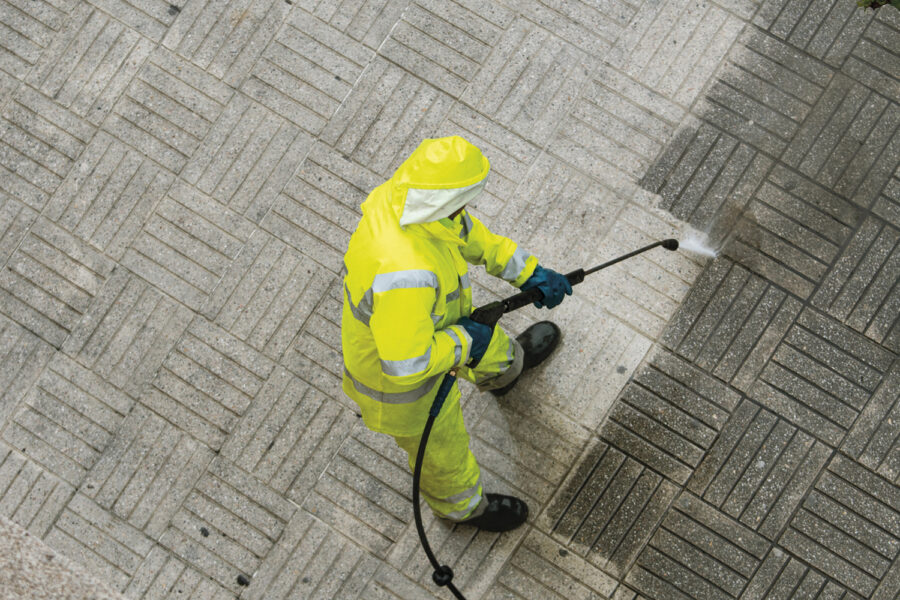 trabajador limpieza con una manguera fregando la calle