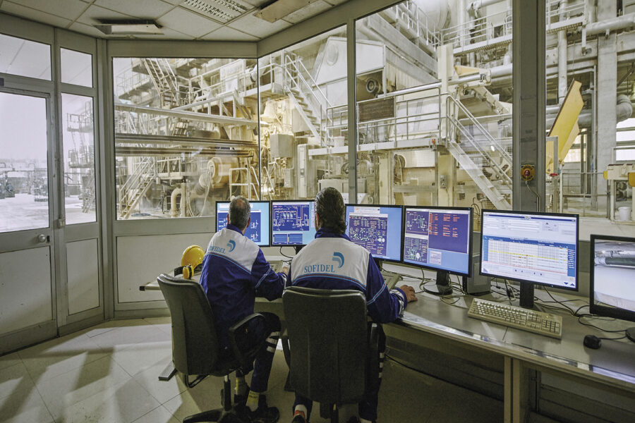 dos trabajadores de Sofidel monitorizando cuatro ordenadores con andamios y estructuras de fondo