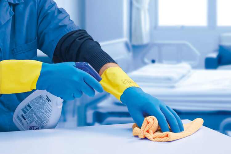 persona con guantes limpiando una superficie con un dispensador y un paño