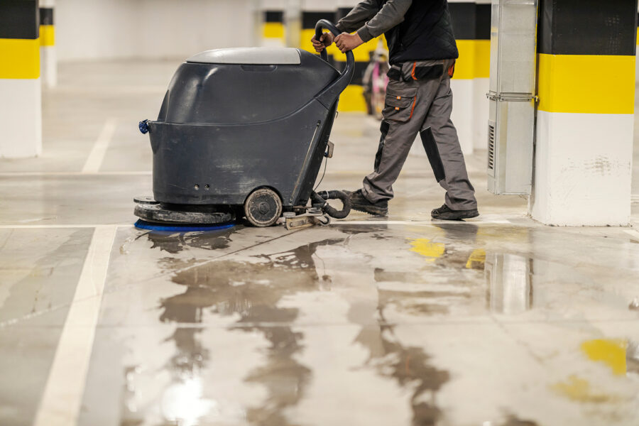 Side view of unrecognizable worker washing garage parking with washing machine.
